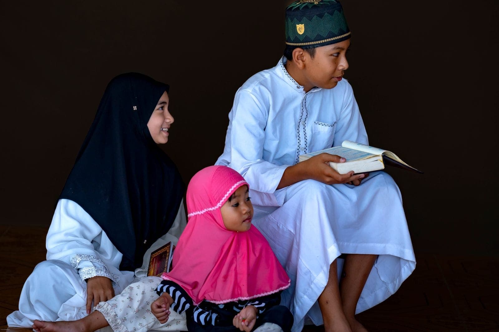 Three children sitting together with a Quran