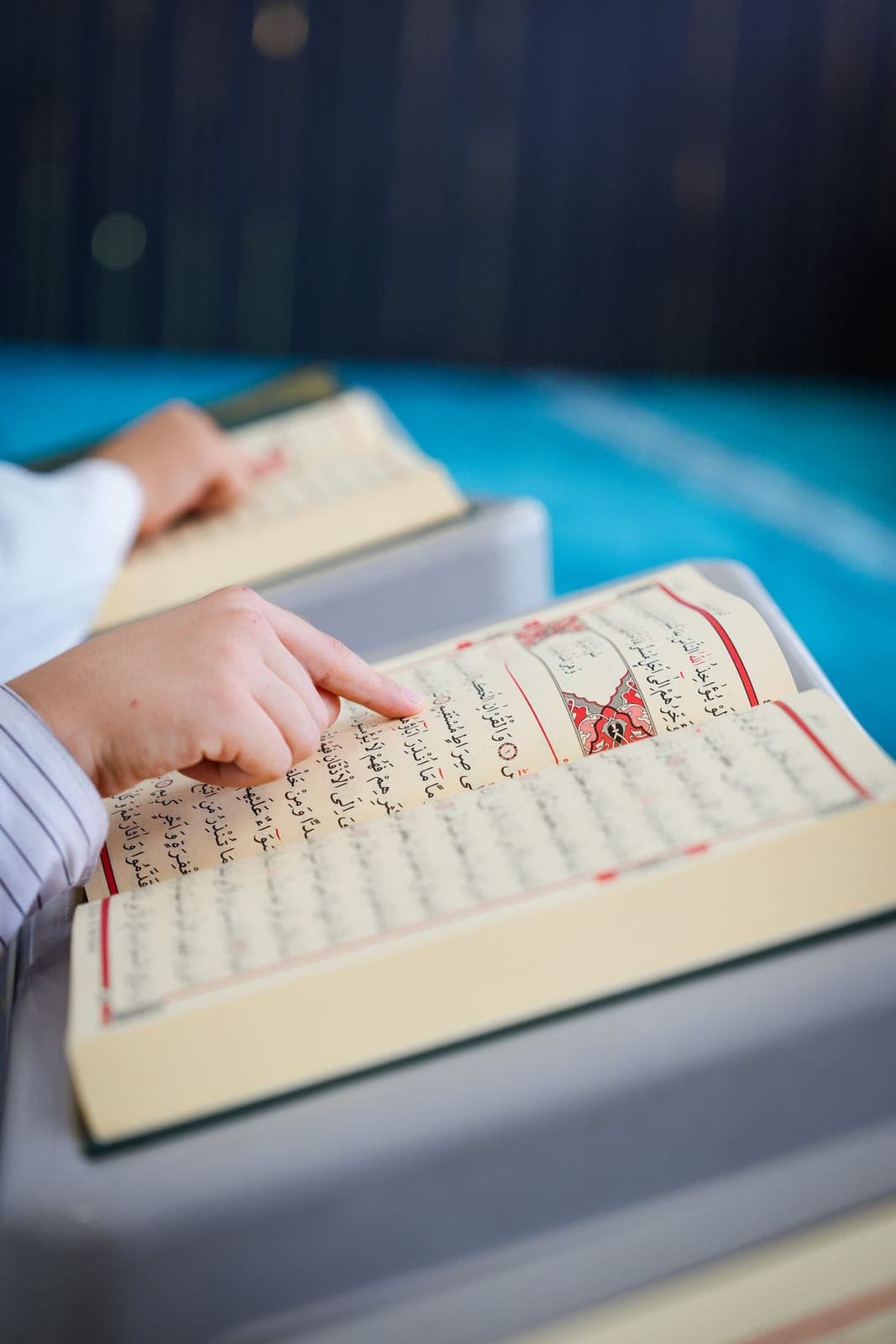 A child pointing to each letter while reading an open Quran