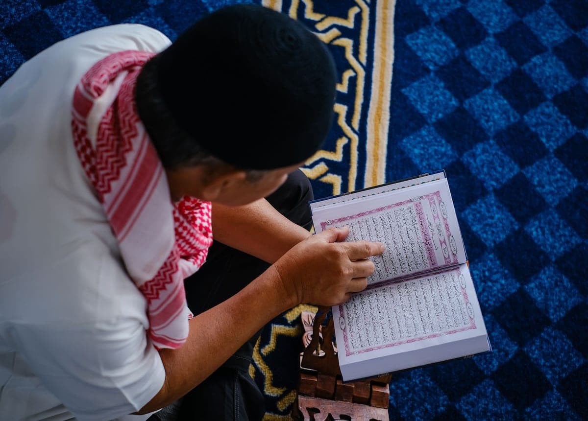 A man following the lines of the Quran with his finger as he reads
